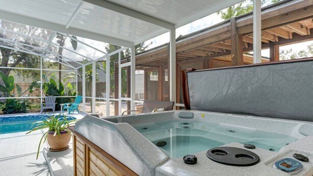 Un jacuzzi con revestimiento de piedra, una terraza de madera y un cerramiento de vidrio.