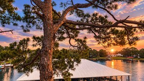 A dock with boats, a covered structure, and a sunset over water. - Amazing view of Grand Lagoon and Walk to Beach (Panama City Beach)