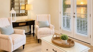A room with a ceiling fan, a mirror, two striped chairs, a white dresser, and a window with blinds. - Amazing view of Grand Lagoon and Walk to Beach (Panama City Beach)
