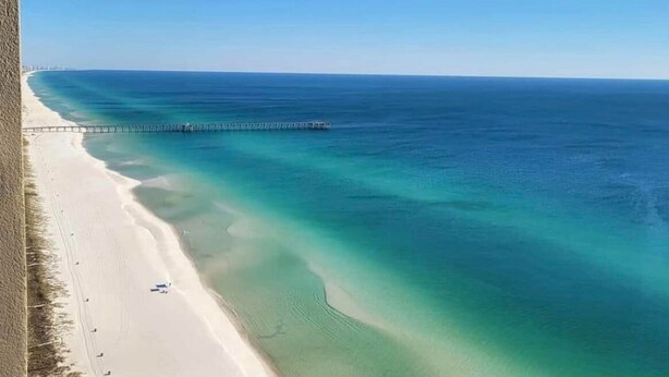 A beach with clear turquoise waters, a sandy shore, and a pier extending into the sea. - Amazing view of Grand Lagoon and Walk to Beach (Panama City Beach)