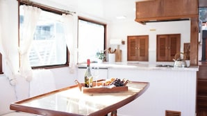 A cozy kitchen with a wooden table, a window with curtains, and a tray of fruits and drinks.