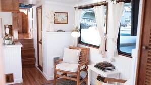 A cozy interior with a wooden chair, a small table with books, a lamp, and a window with curtains.