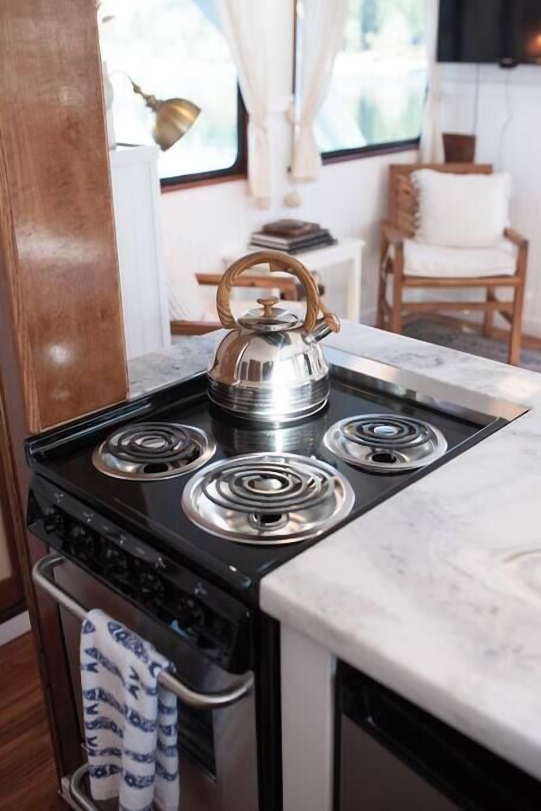 Une cuisine équipée d’une cuisinière, d’une bouilloire et d’une fenêtre avec des rideaux.
