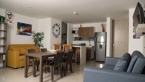 A modern living room with a yellow sofa, a blue couch, a dining table with chairs, a kitchen area with a refrigerator, microwave, and cabinets. - ESTADIA RENTA 302 (Santa Fe de Antioquia)
