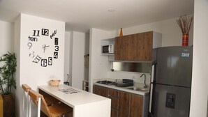 A modern kitchen with a central island, wooden cabinets, stainless steel appliances, and a wall clock. - ESTADIA RENTA 302 (Santa Fe de Antioquia)