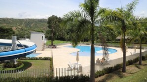 A pool area with a blue and white water slide, palm trees, and a fenced deck with lounge chairs. - ESTADIA RENTA 302 (Santa Fe de Antioquia)