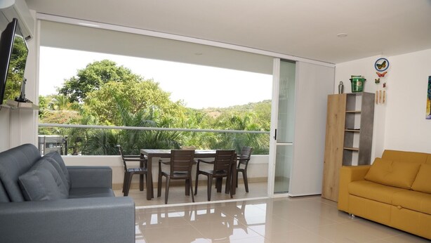 A modern living room with a balcony, a sofa, a dining table with chairs, and a yellow armchair. - ESTADIA RENTA 302 (Santa Fe de Antioquia)