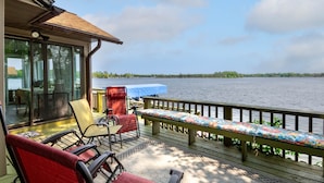 Een terras met buitenmeubilair, uitzicht op een meer en een overdekt gedeelte met een tafel en stoelen.