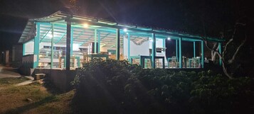 Una casa con cerramiento de vidrio, un porche con sillas y un interior bien iluminado.