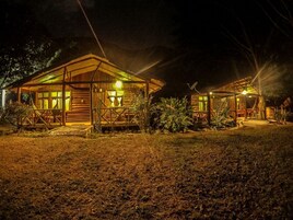 Un edificio de estilo cabaña de madera con un porche y una pequeña terraza, rodeado de follaje.