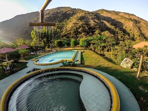 A pool with a waterfall feature, surrounded by lush greenery and hills in the background. - Willka Eco Farm (Peñaherrera)