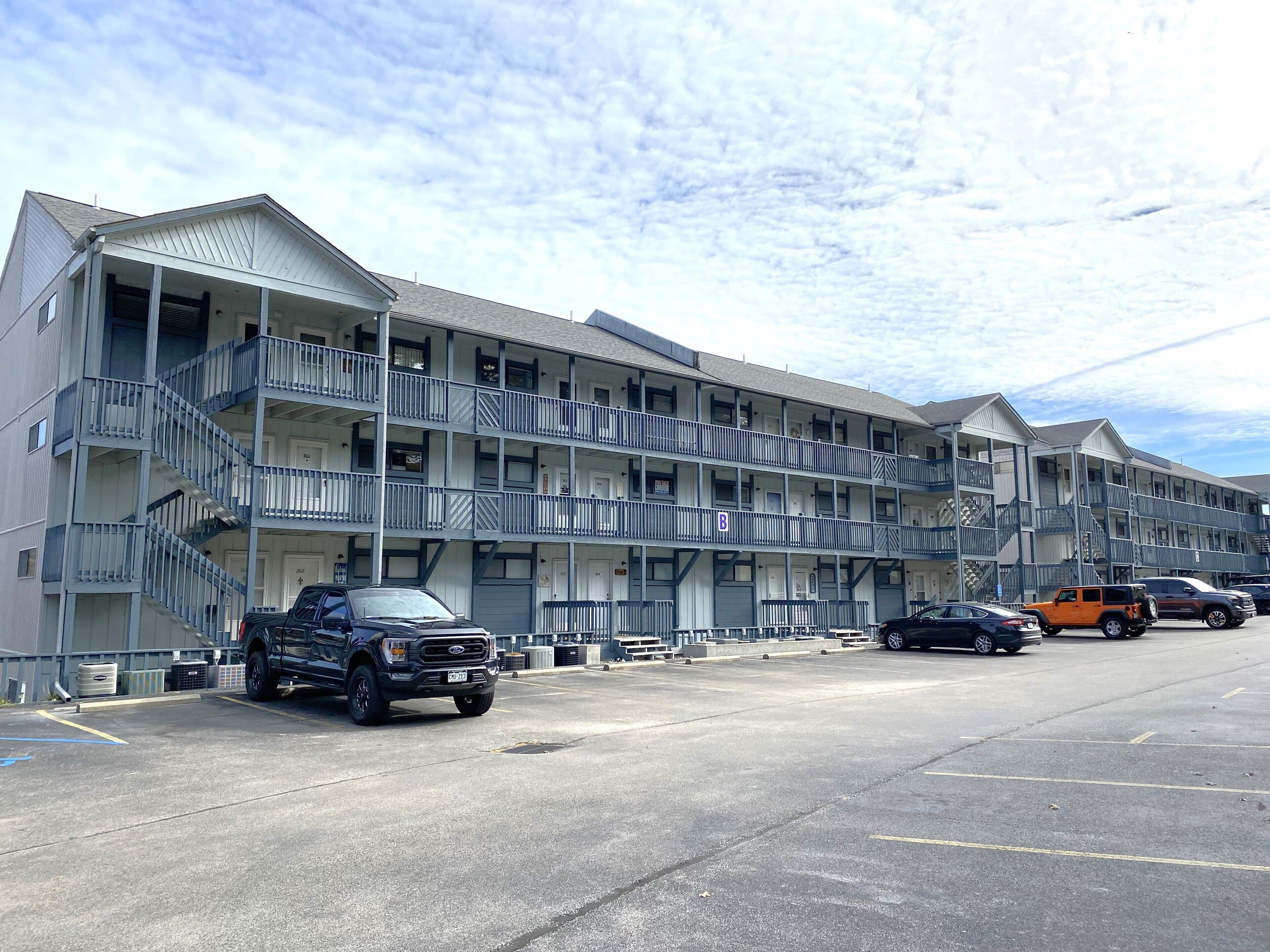 Un motel de varios pisos con balcones, estacionamiento y cielo despejado.