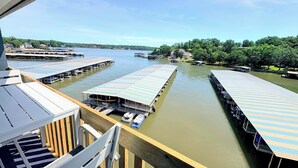 A docked boat with a covered area, a pier with a railing, and a view of the water and surrounding greenery. - B Lakefront! Remodeled, Boat Slip, Ramp, Patio Views, Sleeps 4, Pool, Kitchen (Osage Beach)