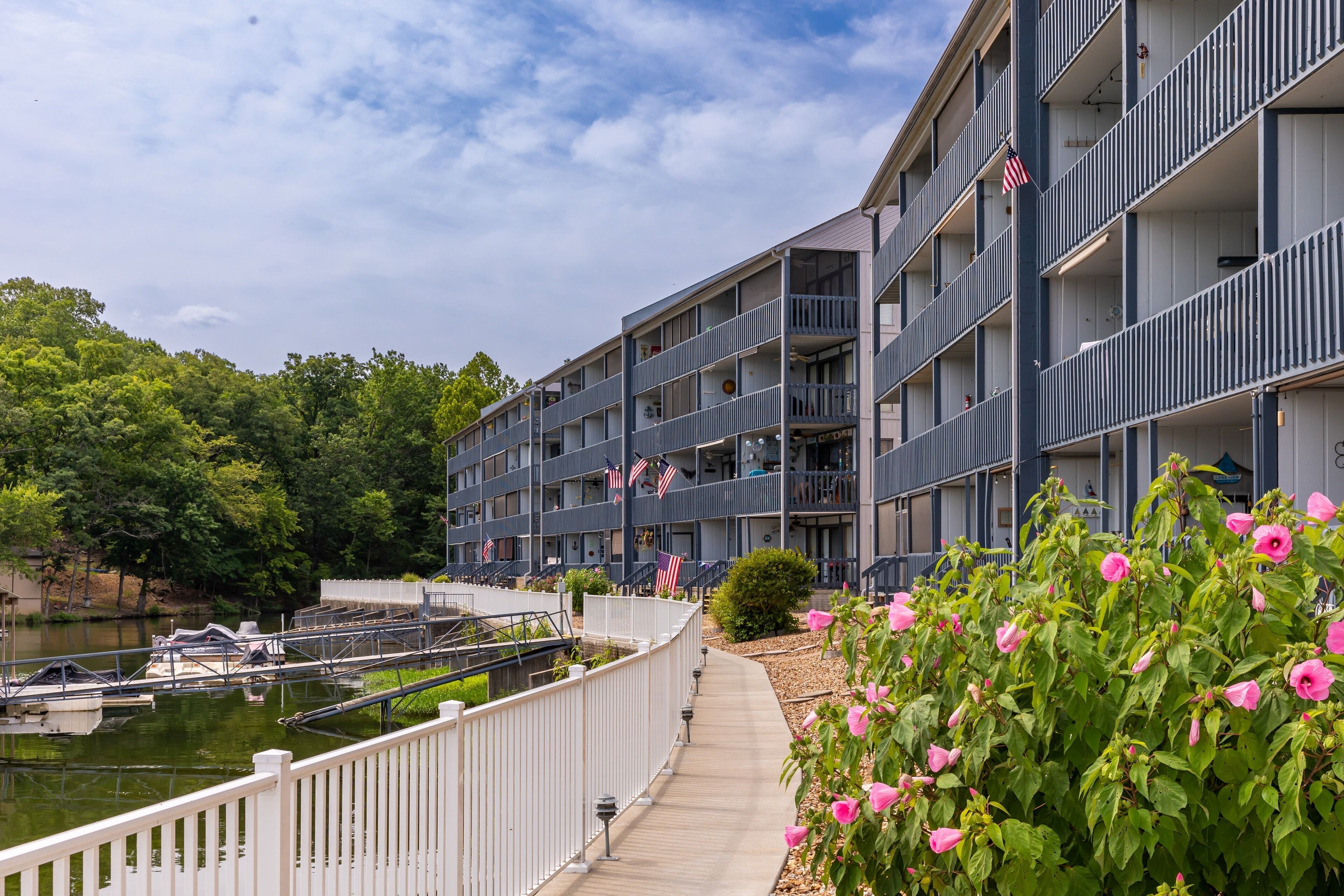 A multi-story building with balconies, a pathway, and a body of water with boats.