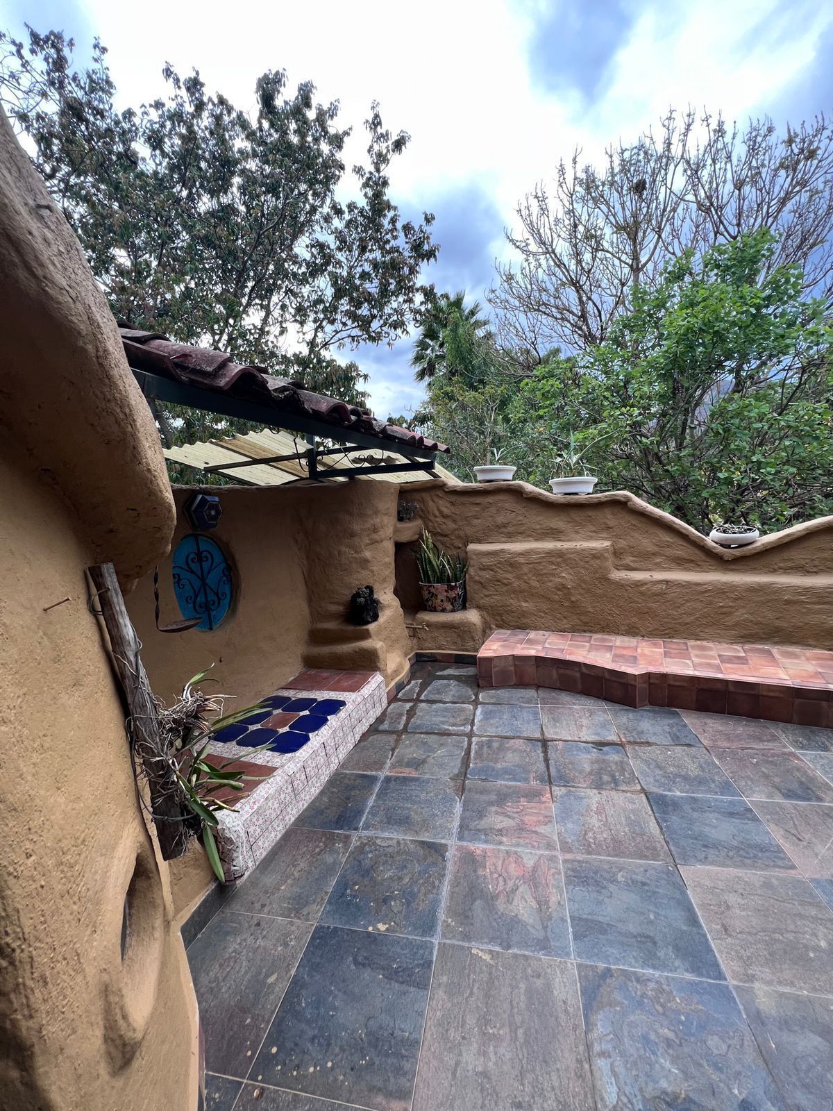 Un espace patio avec des carreaux de pierre, un mur rustique agrémenté d’un carrelage décoratif et des plantes en pot.