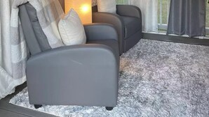 Hyggelig siddekrog med to grå sofaer og en stor gulvlampe, med træloft og store vinduer med gardiner.
