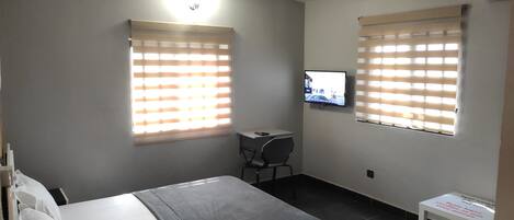 A hotel room with a bed, a desk, and a television mounted on the wall.
