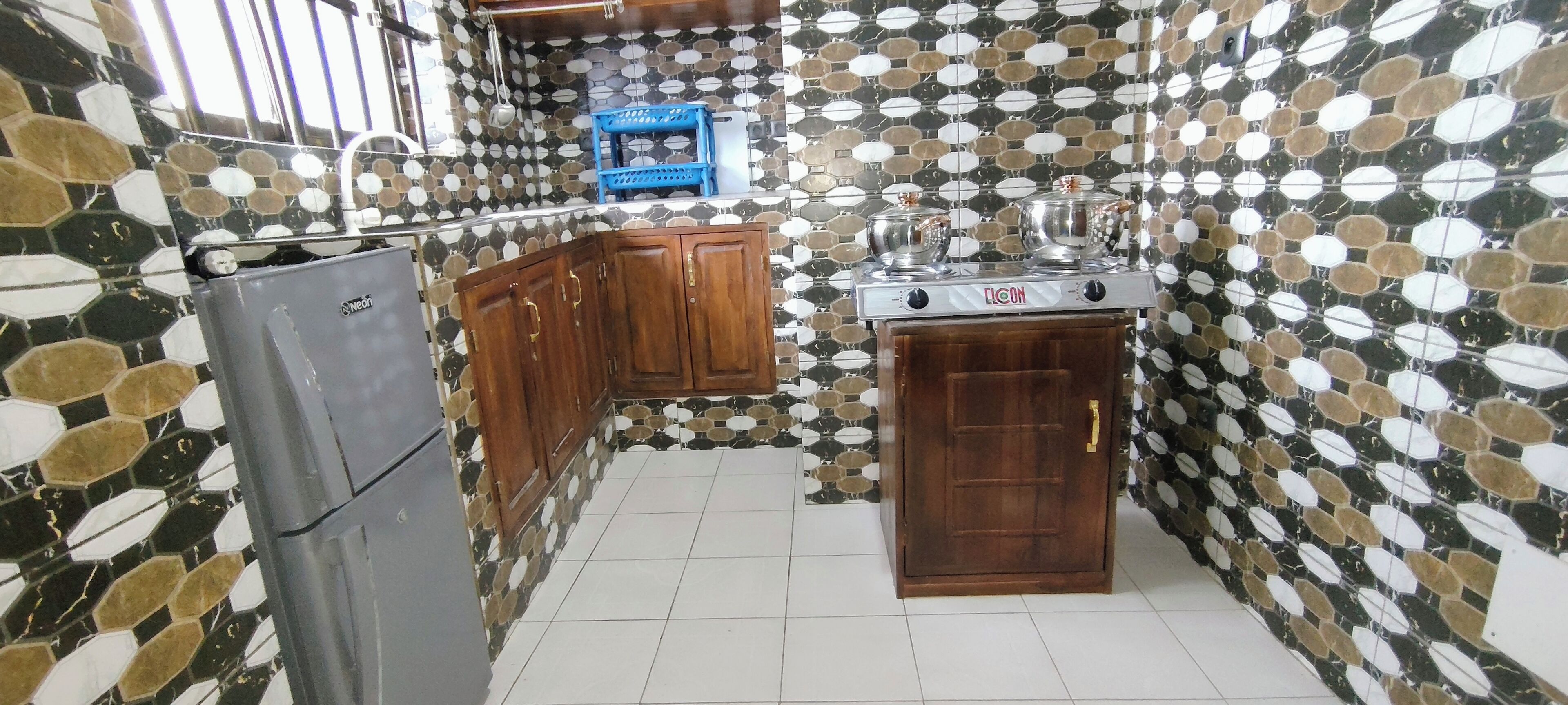 A kitchen with a refrigerator, wooden cabinets, a stove, and a blue shelf.