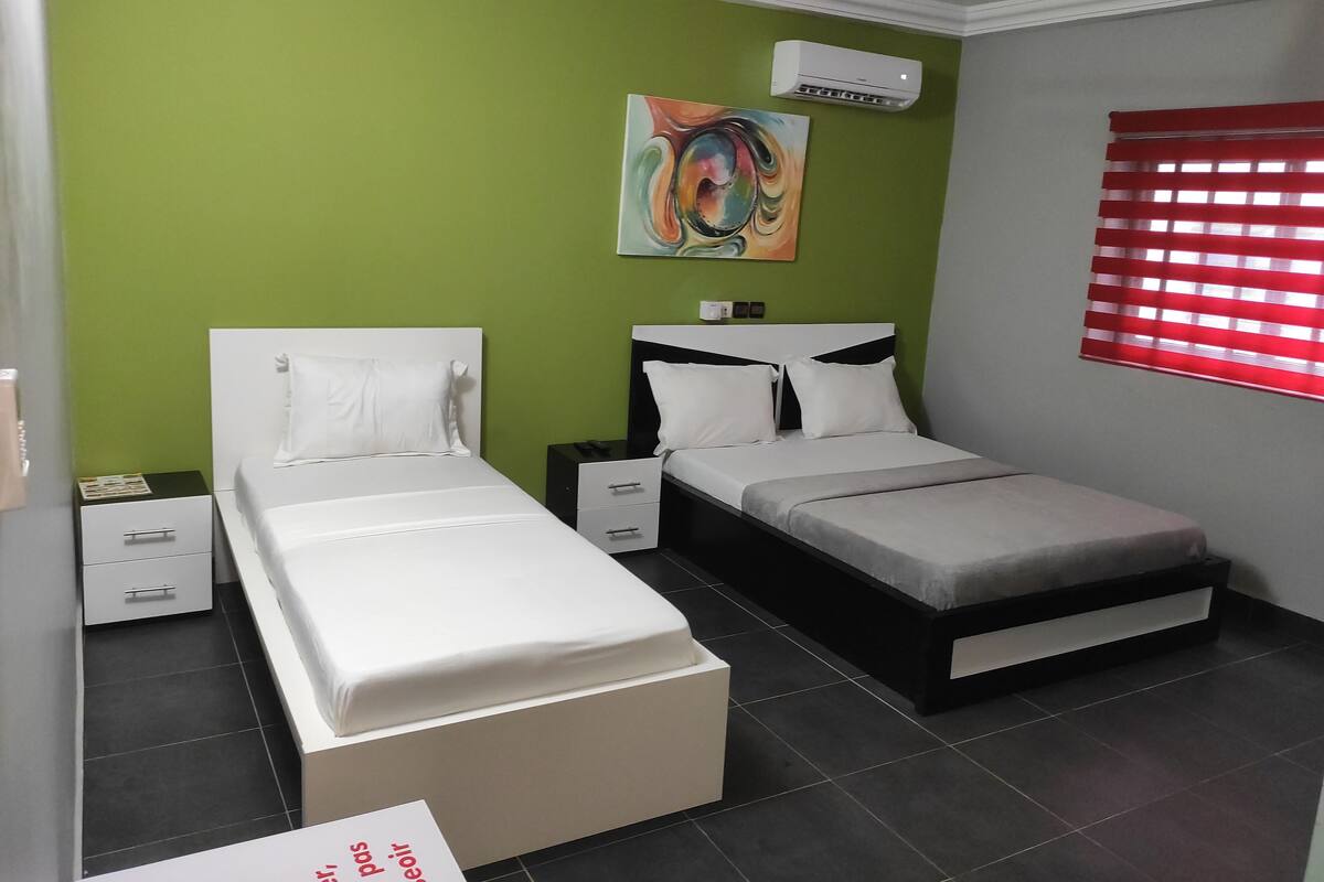 A room with two beds, a nightstand, a drawer unit, and a painting on the wall.