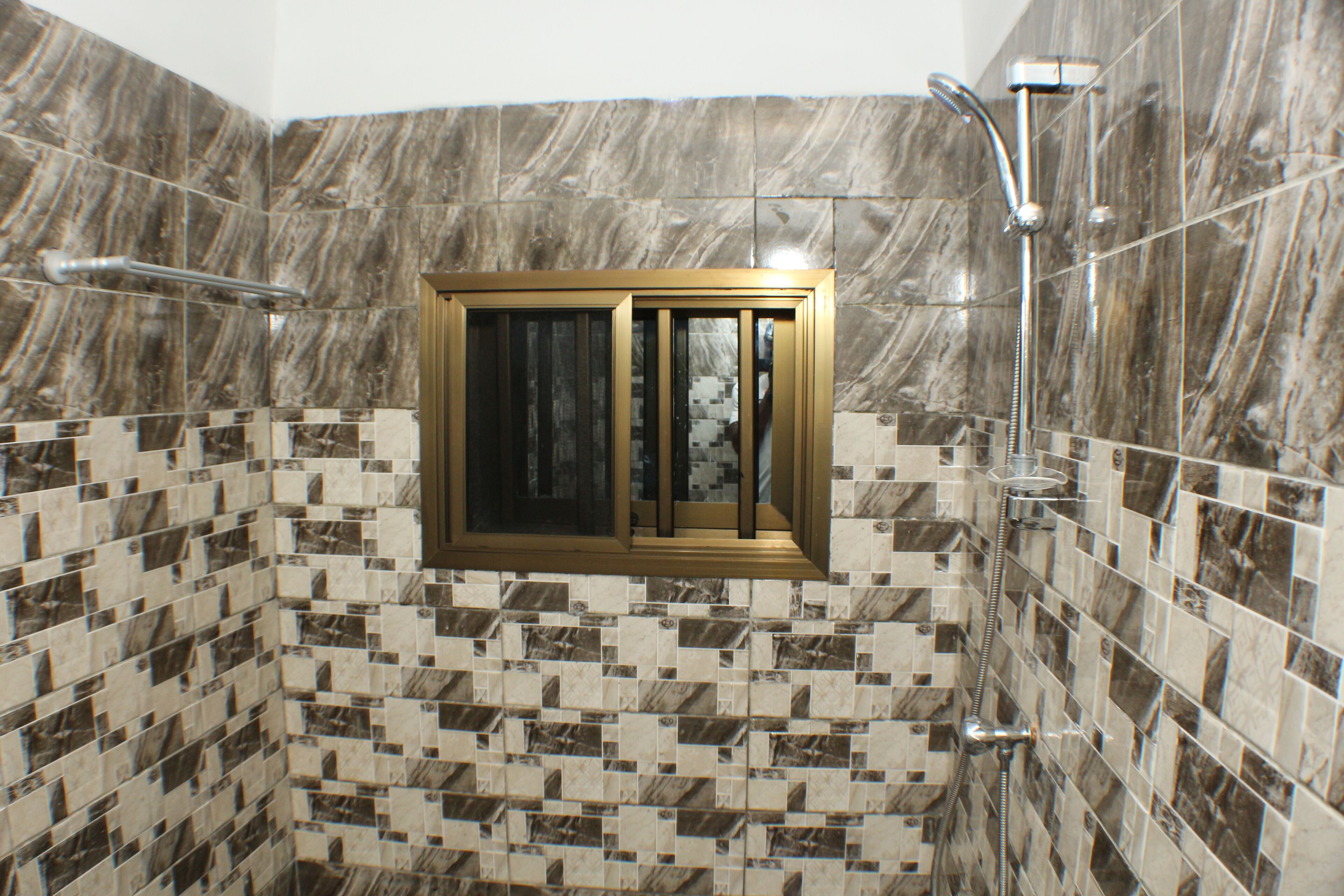 A bathroom with a shower area, tiled walls, and a window with a wooden frame.