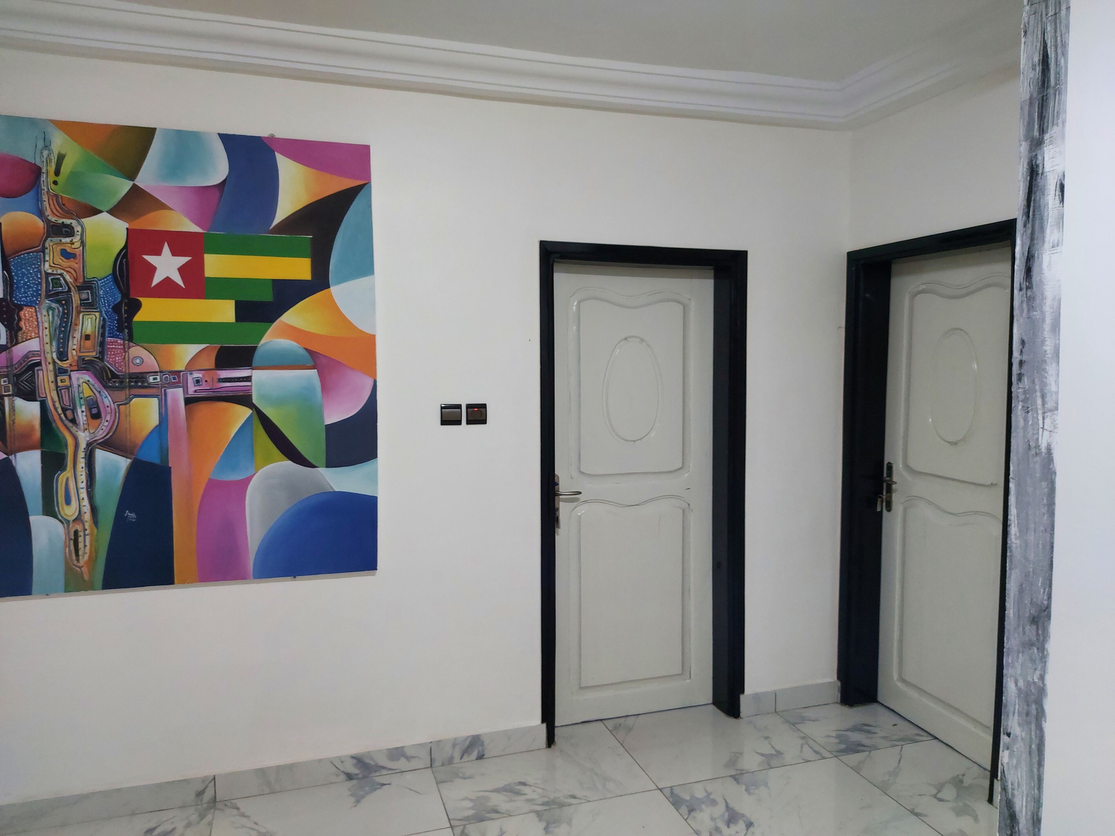 A hallway with two doors, a colorful abstract painting on the wall, and a marble floor.