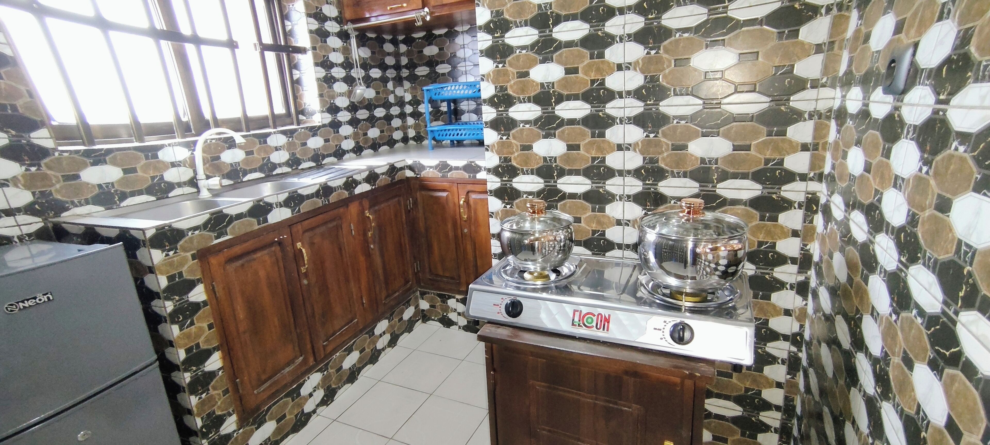 A kitchen with a gas stove, wooden cabinets, a blue chair, and a neon refrigerator.