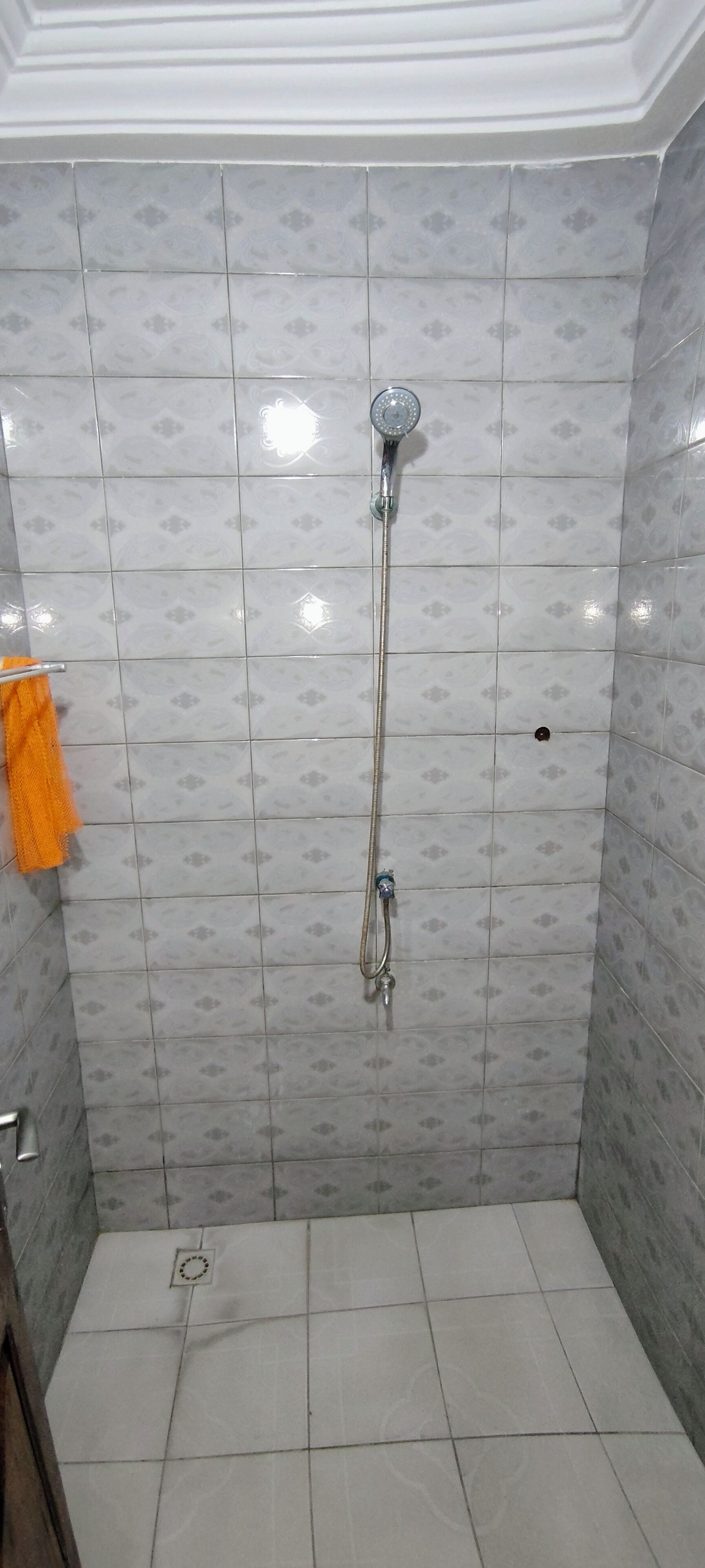 A shower with a handheld showerhead and a wall-mounted faucet, tiled walls, and a small vent on the floor.