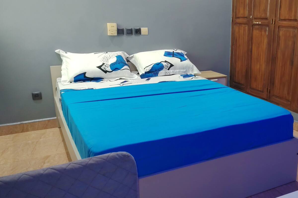 A bedroom with a bed, a wardrobe, a bedside table, and a chair.