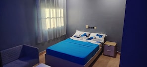 Een slaapkamer met een bed, een stoel, een nachtkastje en een raam met gordijnen.