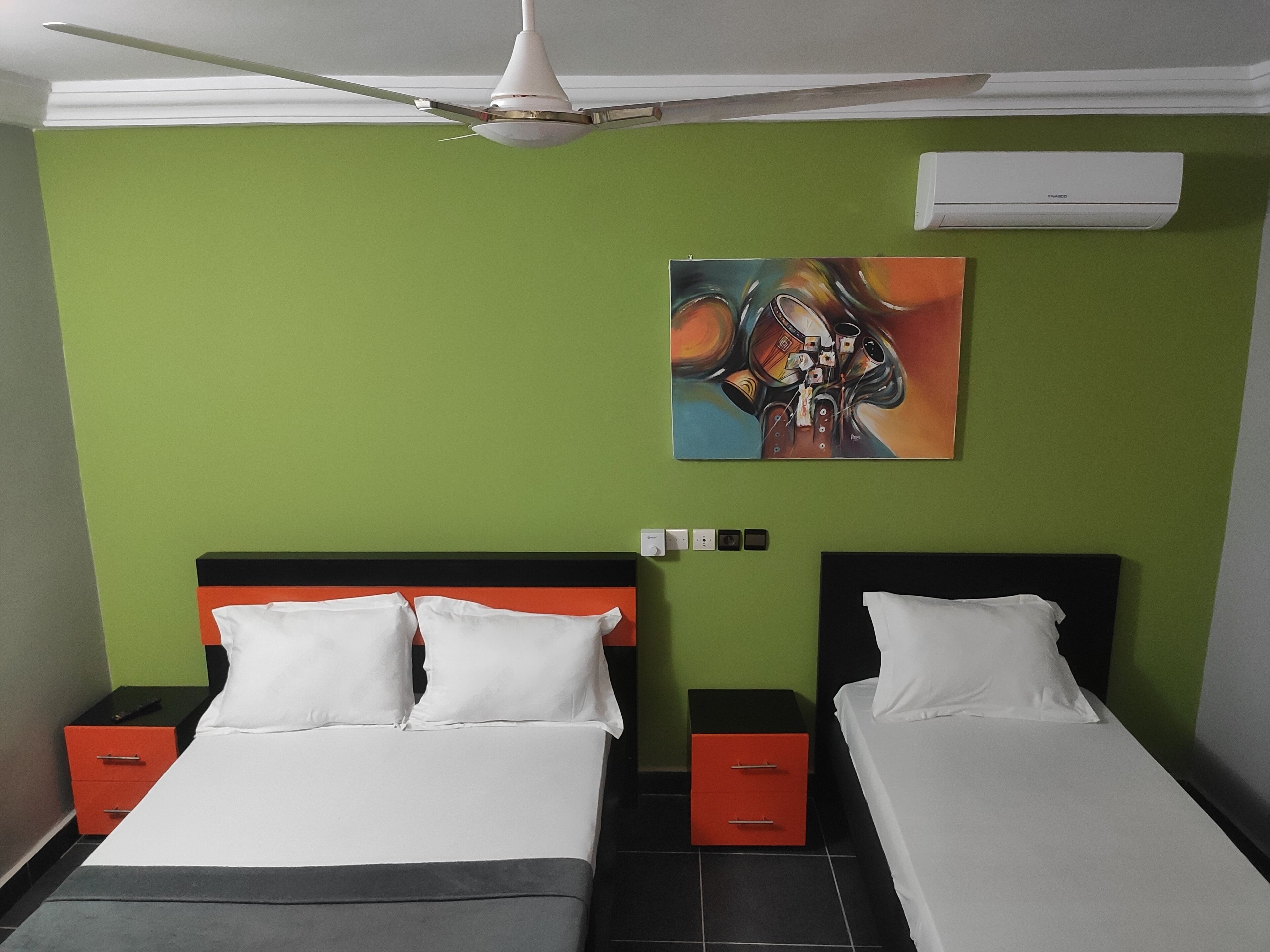 Une chambre avec deux lits, un ventilateur de plafond, un climatiseur et un tableau au mur.