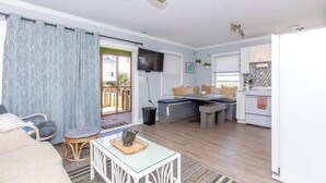 A compact living space with a sofa, a small table with a decorative item, a dining area with a bench, a kitchen with white cabinets, and a ceiling fan. - Overlook the Intracoastal and walk to the beach! (North Topsail Beach)