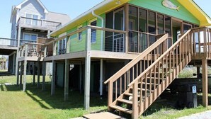 A two-story house with a green and yellow exterior, a wooden deck, and a staircase leading to the upper level. - Overlook the Intracoastal and walk to the beach! (North Topsail Beach)