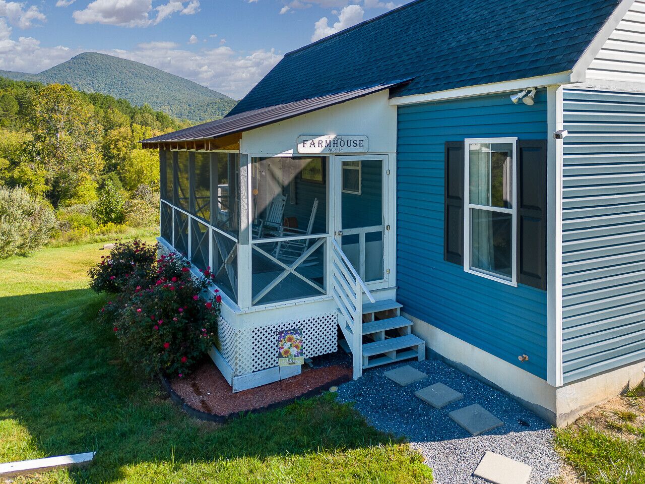 Une ferme avec un porche couvert, une enseigne indiquant « Ferme », et une vue sur une montagne en arrière-plan.