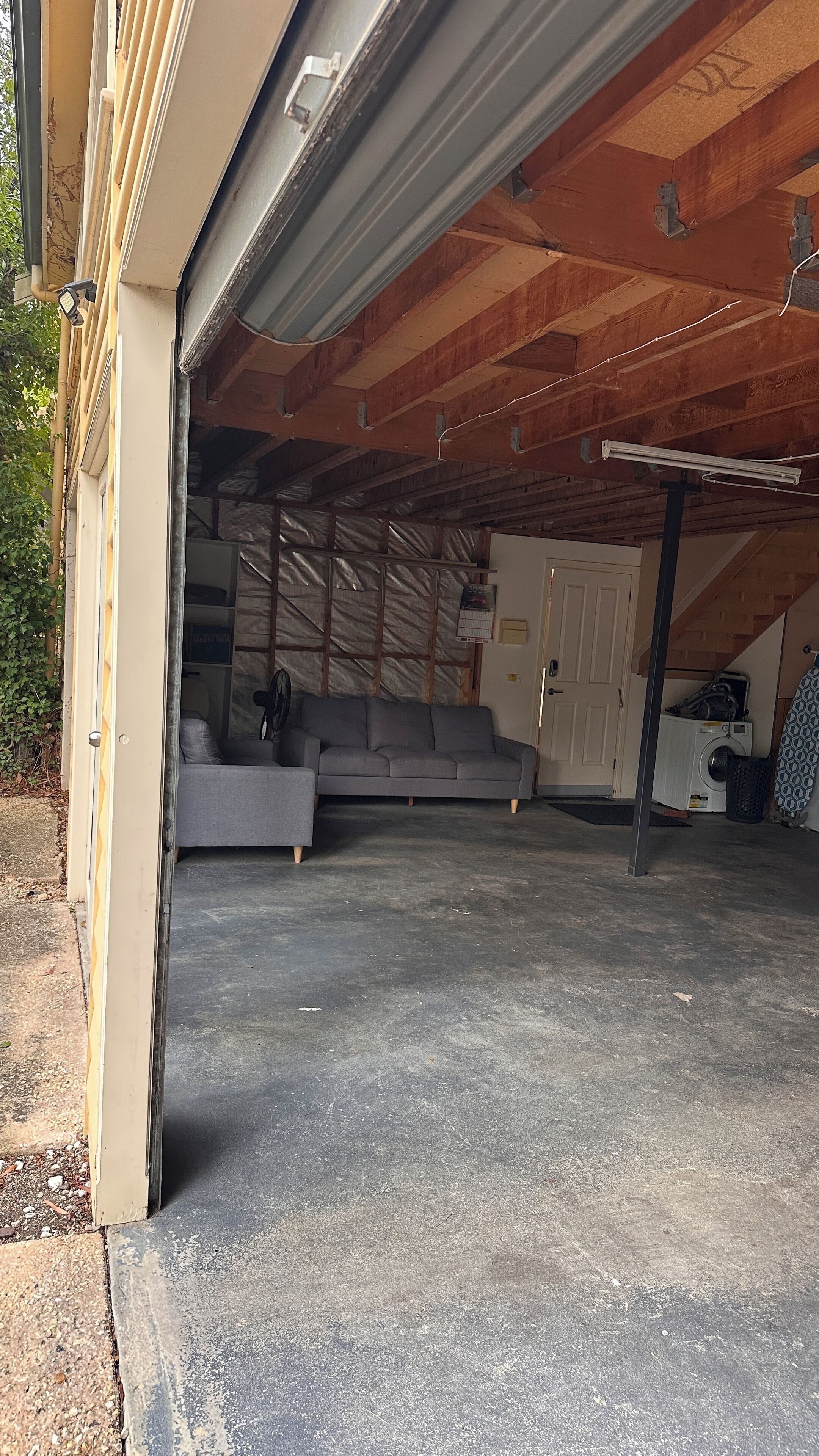 A garage with a concrete floor, a grey sofa, and a washing machine.