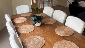 Un coin repas avec une table en bois, des chaises blanches et des sets de table en fibres tressées.