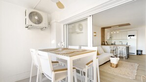 A modern kitchen with white cabinets, a dining area with white chairs and a wooden table, and a ceiling fan.