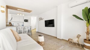 A modern living room with a sofa, a dining area with chairs, a TV mounted on the wall, and a large potted plant.