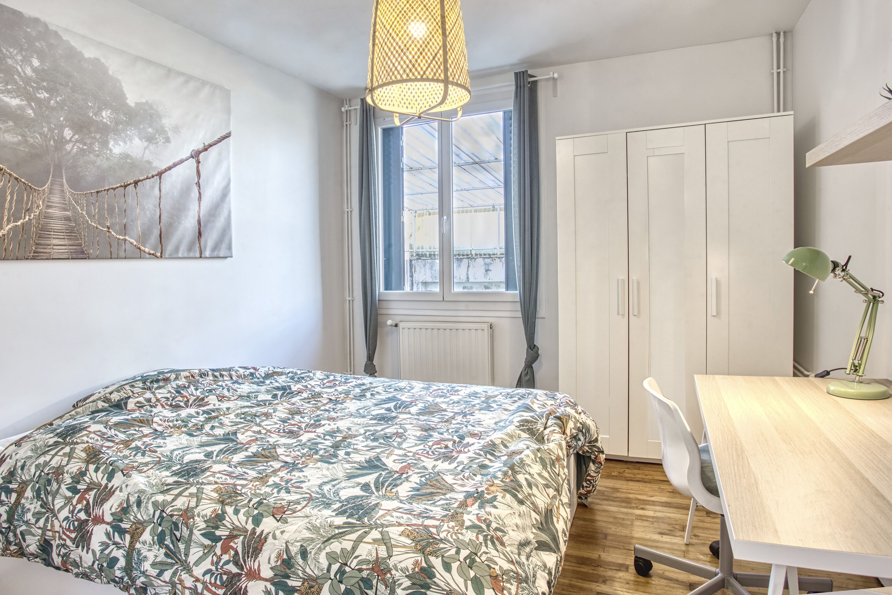 A bedroom with a bed, a desk, a chair, a window, and a painting on the wall.