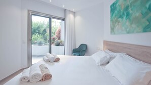 Ein modernes Hotelzimmer mit einem großen Bett, Blick ins Grüne durch die Schiebetür, einem türkisfarbenen Sessel und einem großen, abstrakten Gemälde an der Wand.