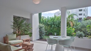 Ein modernes Wohnzimmer mit einer Couch, Sesseln und einem Esstisch. Ein großes Fenster bietet Blick auf Grünflächen und Gebäude.