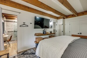 A bedroom with a bed, a TV mounted on the wall, wooden beams on the ceiling, and a door leading to another room. - Cozy & Chic Lake Arrowhead Cabin w/ Deck! (Lake Arrowhead)