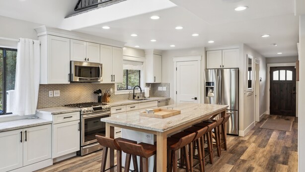 Una cocina moderna con armarios blancos, electrodomésticos de acero inoxidable, una isla grande con taburetes y un tragaluz.