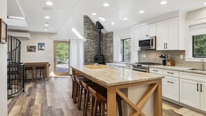 Una cocina moderna con una isla central, armarios blancos, una pared decorativa de piedra y una estufa negra.