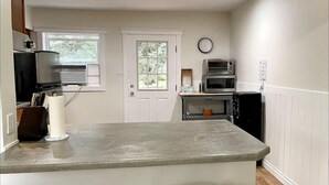 A kitchen with a central island, two bar stools, a microwave, a toaster, and a clock on the wall.