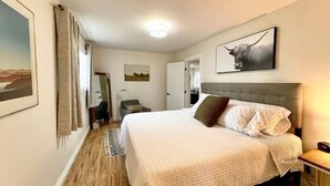 A bedroom with a large bed, a headboard, a bedside table, a lamp, and a painting on the wall.