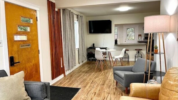 A modern living room with a sofa, a coffee table, and a television. There is a dining area with a table and chairs.