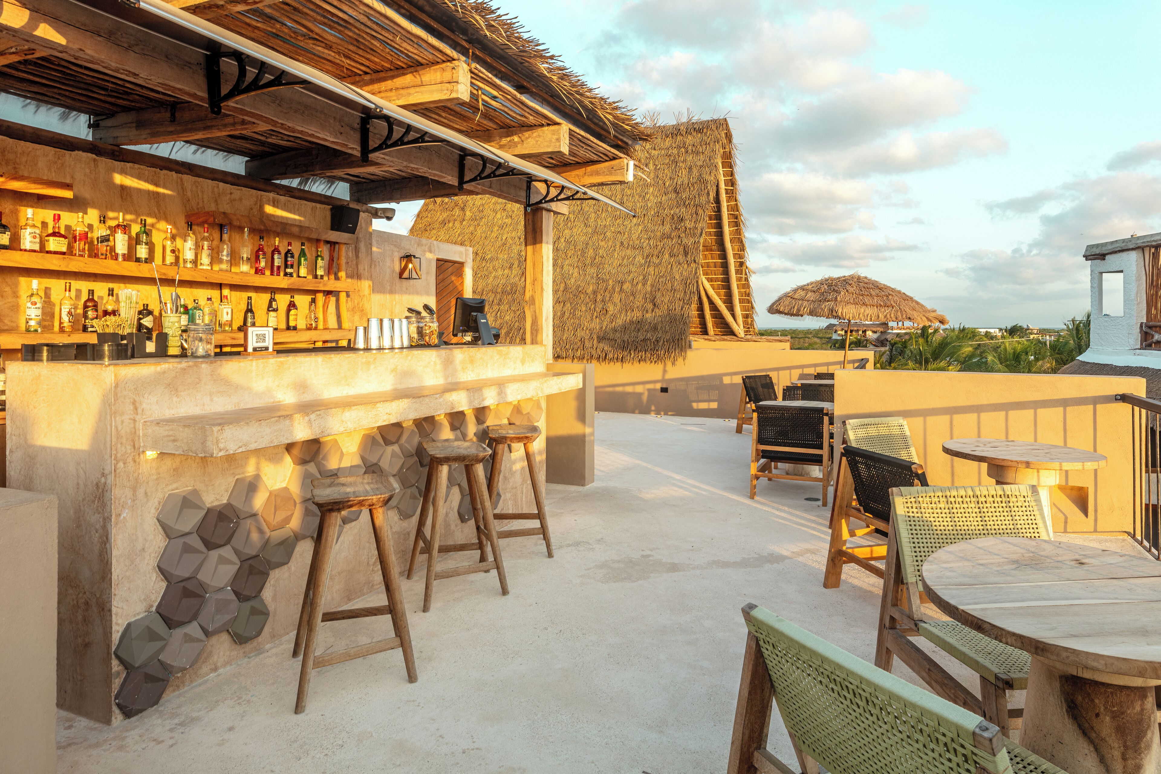 A bar area with stools, a counter with bottles, and a thatched roof structure.