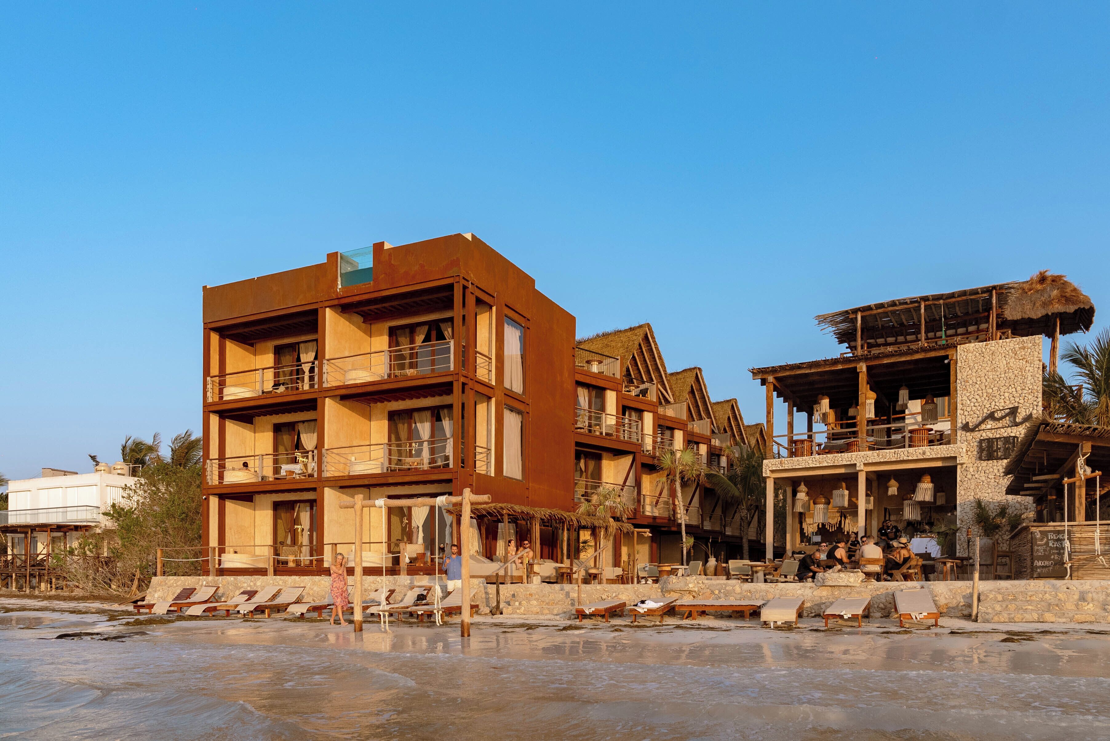 A beachfront hotel with multiple balconies, outdoor seating areas, and a poolside lounge.