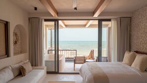 Una habitación de hotel con una cama grande, un sofá, un balcón con vista al mar y un ventilador de techo.