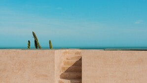 Una escalera de hormigón conduce a un balcón con vistas a un cielo azul despejado y un mar tranquilo.